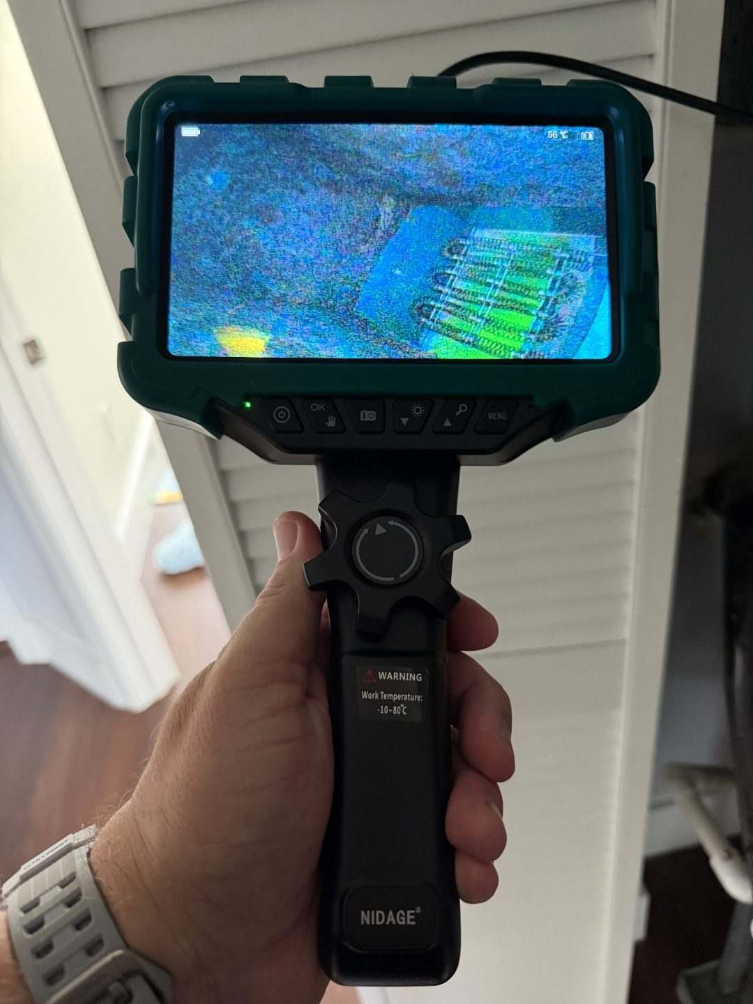 Hand holding a borescope camera near a closet door, displaying a scan on its screen