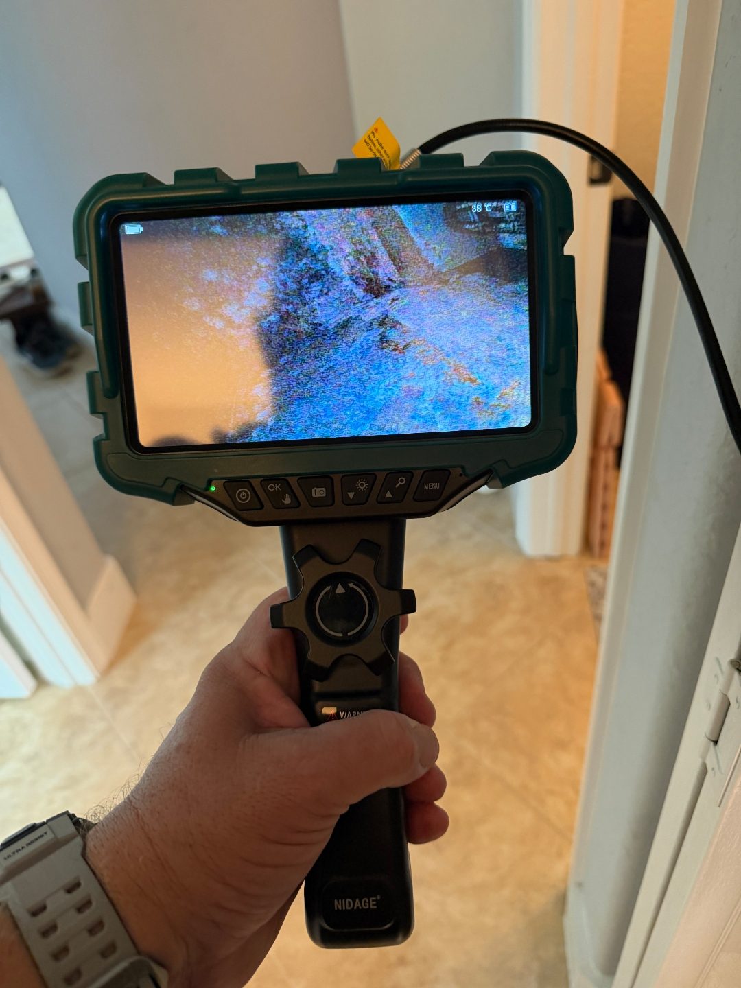 Hand holding a borescope camera displaying a scan in a hallway, a second angle of the same scene