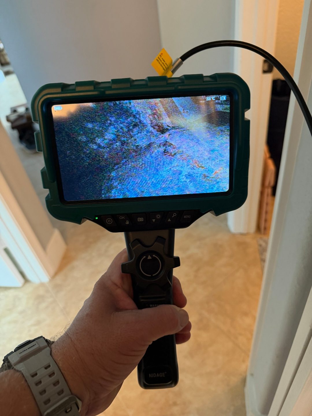 Hand holding a borescope camera displaying a scan in a hallway, a third angle of the same scene