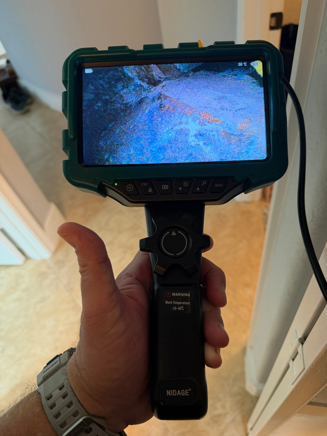 Hand holding a borescope camera displaying a scan in a hallway, a fourth angle of the same scene