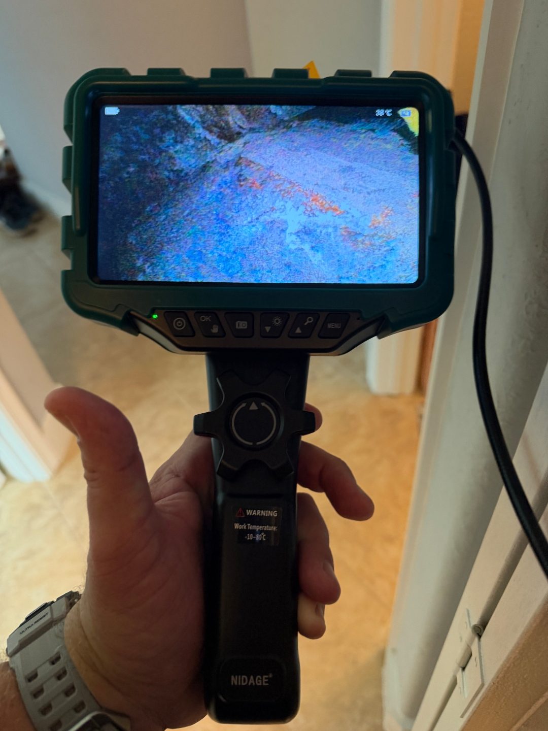 Hand holding a borescope camera displaying a scan in a dim hallway, a fifth angle of the same scene