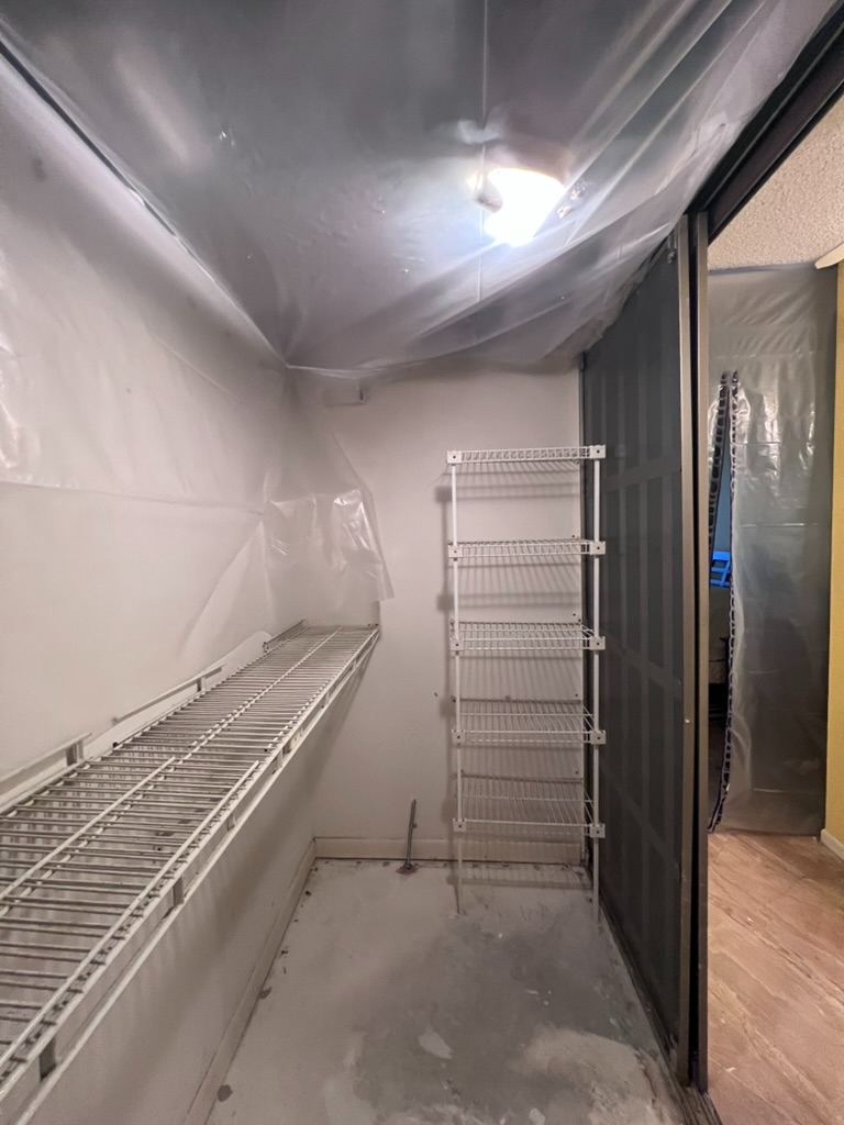 Wide view of a closet ceiling showing dark, discolored staining above the remediation containment sheeting, indicating remaining mold contamination after remediation work