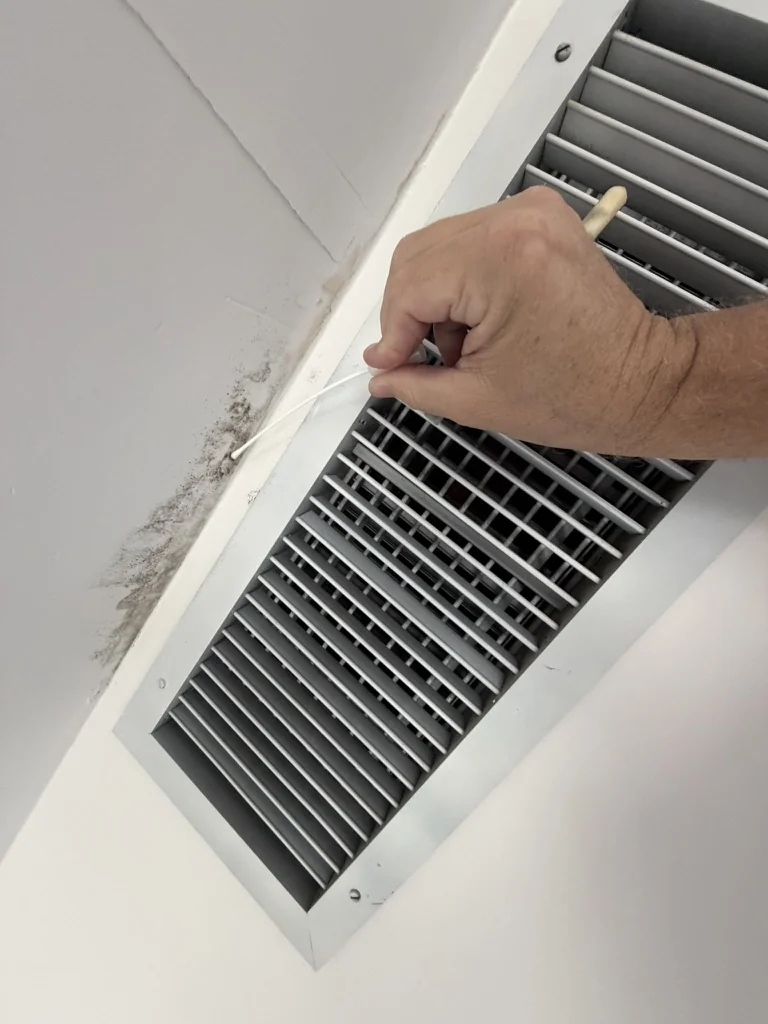 Inspector collecting a surface swab beside a discolored HVAC supply register