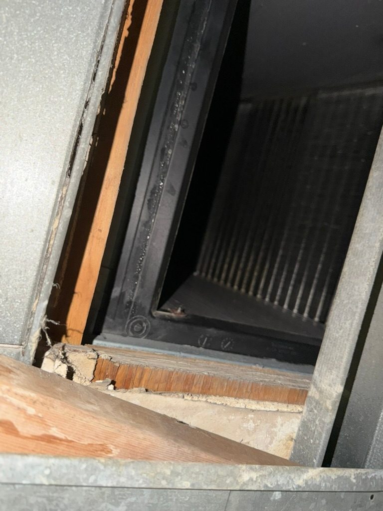 Close-up view into an opening in ductwork showing a heat exchange coil inside
