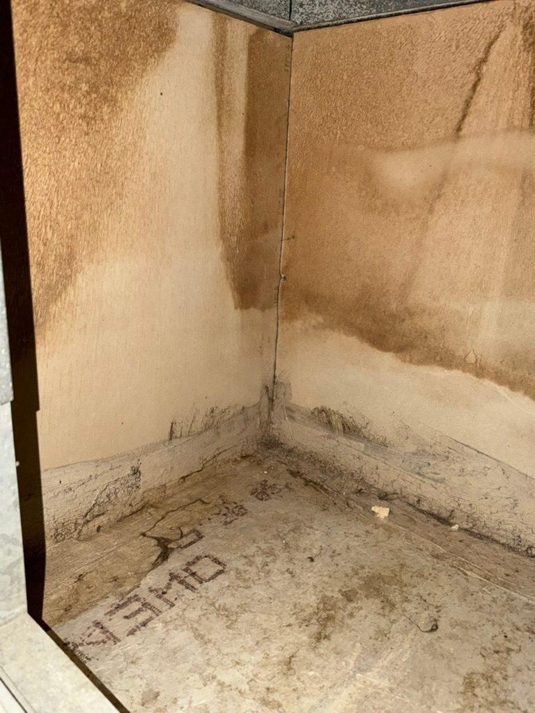 Close-up inside an enclosed wall cavity showing a water staining tide line on panel walls