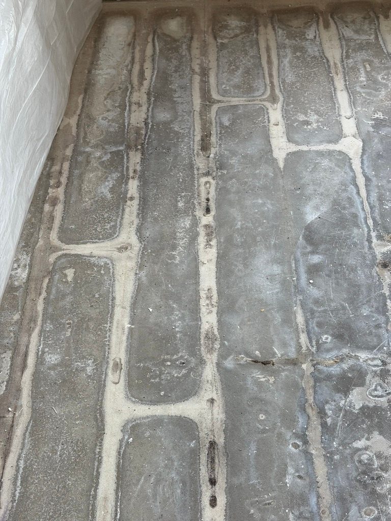 Overhead view of a bare concrete slab showing a tile adhesive ridge pattern after flooring removal