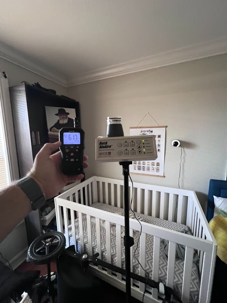 Air sampling pump positioned near a crib during an indoor air quality assessment in a bedroom