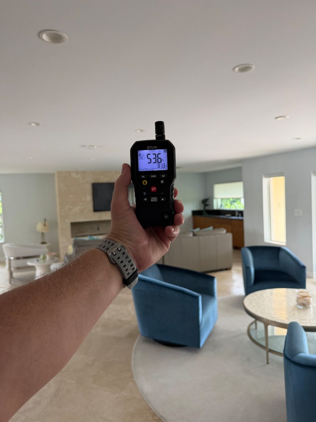 Hand holding a digital moisture meter in a living room near a fireplace