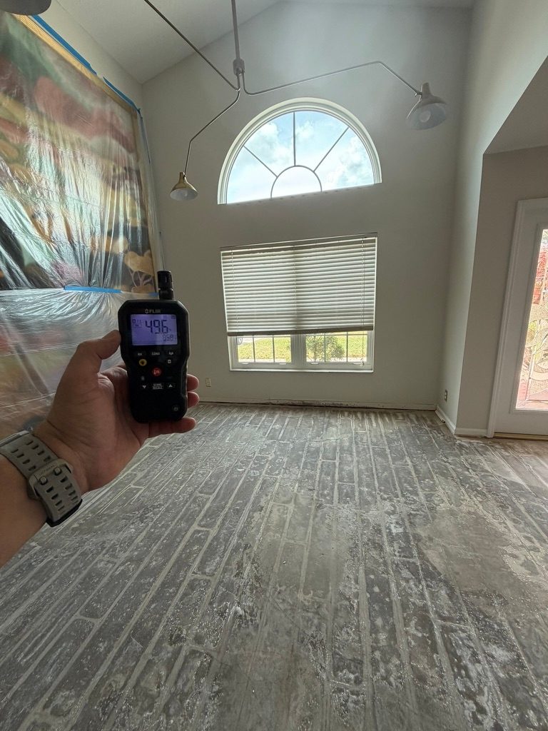 Hand holding a moisture meter in a vaulted great room with an arched clerestory window
