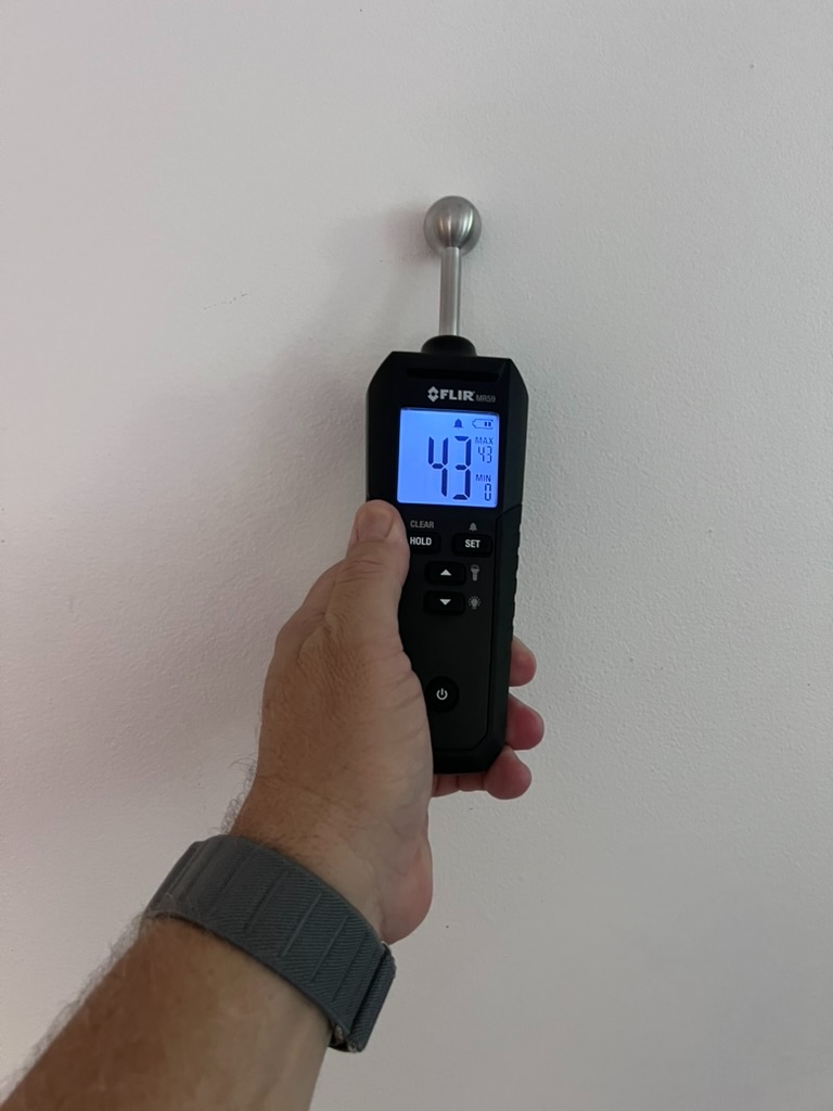 FLIR pin-type moisture meter reading confirming elevated moisture at the wall