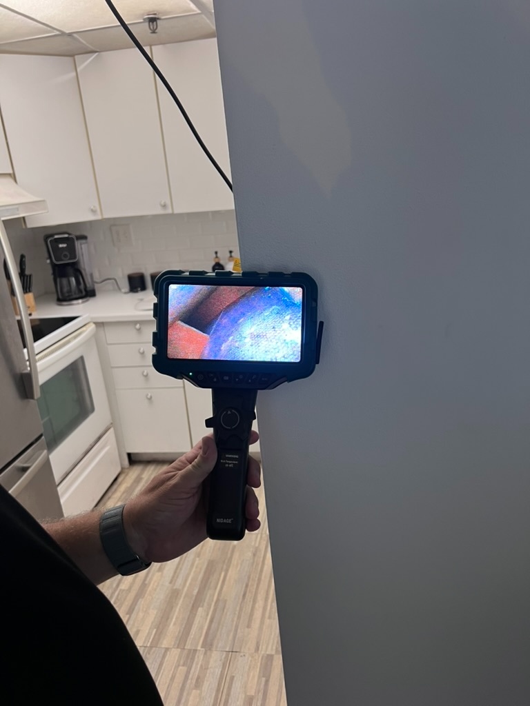 Video borescope camera inserted into a wall opening showing live feed on the handheld monitor