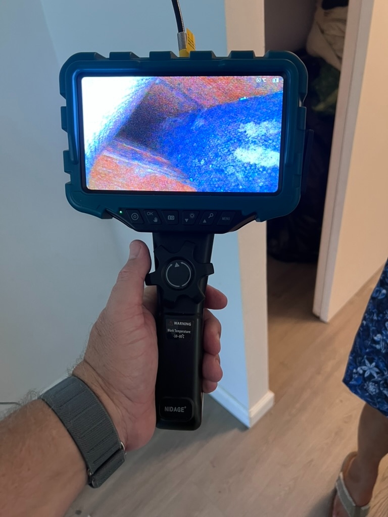 Borescope monitor displaying suspected microbial growth and moisture staining inside the concealed wall cavity