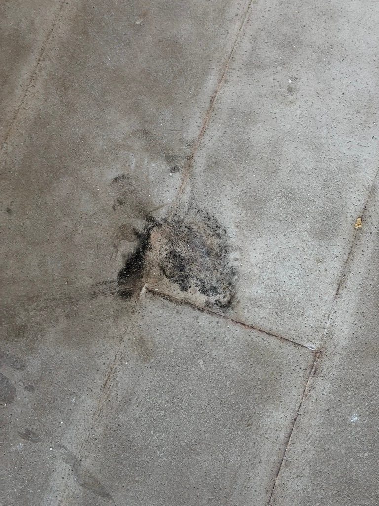 Overhead close-up of a bare concrete slab showing staining concentrated at a control joint