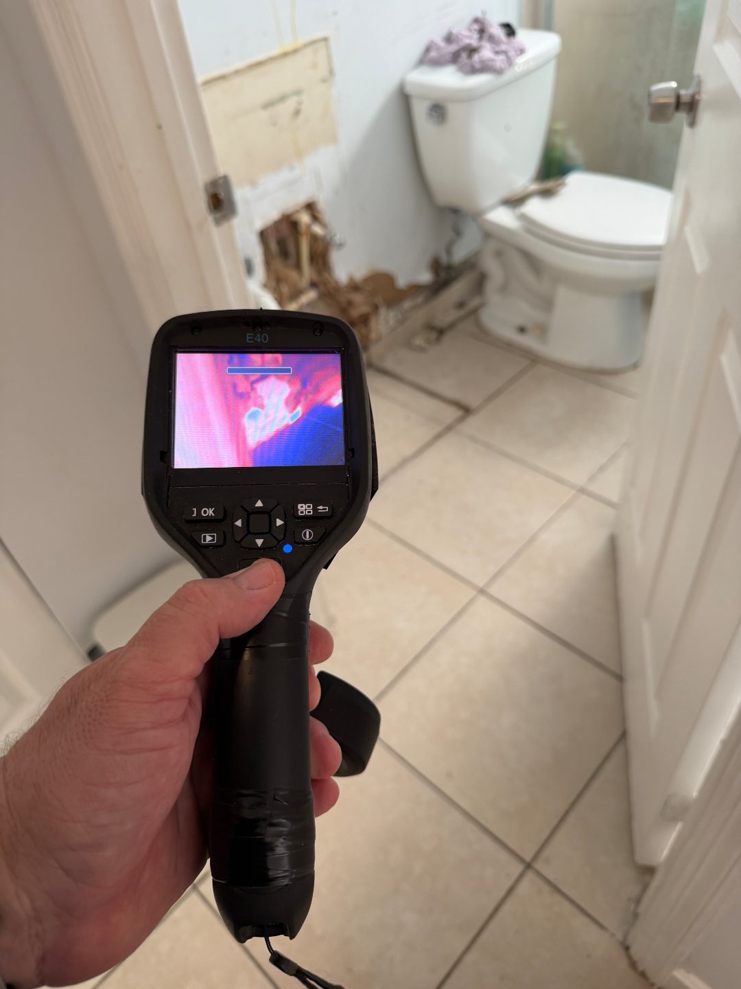 Hand holding a thermal imaging camera near an open bathroom wall section, a third angle of the same scene